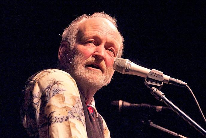 Valdy, a renowned Canadian folk musician, performs on stage with a microphone.