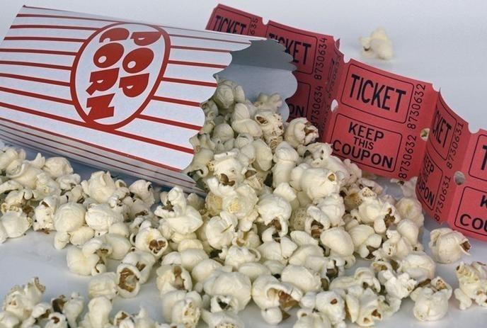 Popcorn spilling out of a box with red movie tickets behind it.