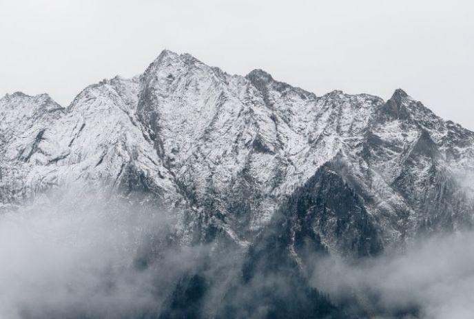 A mountain scenery with snow and clouds under a cloudy sky