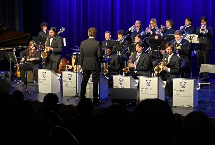 A jazz band performs on stage with a conductor leading. The musicians play saxophones, trumpets, and trombones.