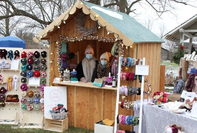 Wooden booth at outdoor market with colorful handmade hair accessories: scrunchies, headbands; sign says