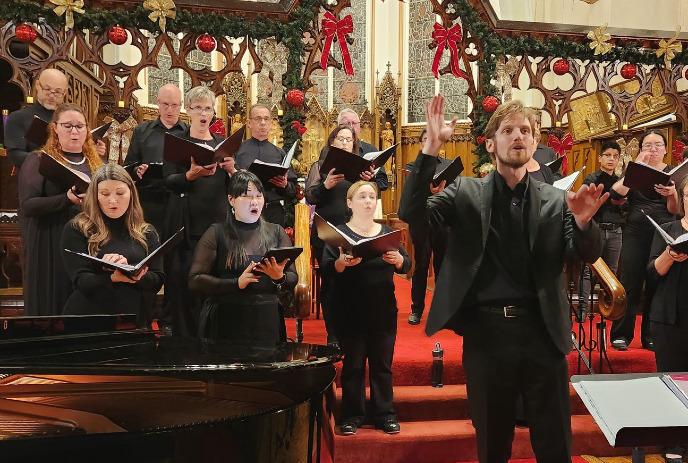 A choir dressed in black performs in a decorated church with a conductor leading them.