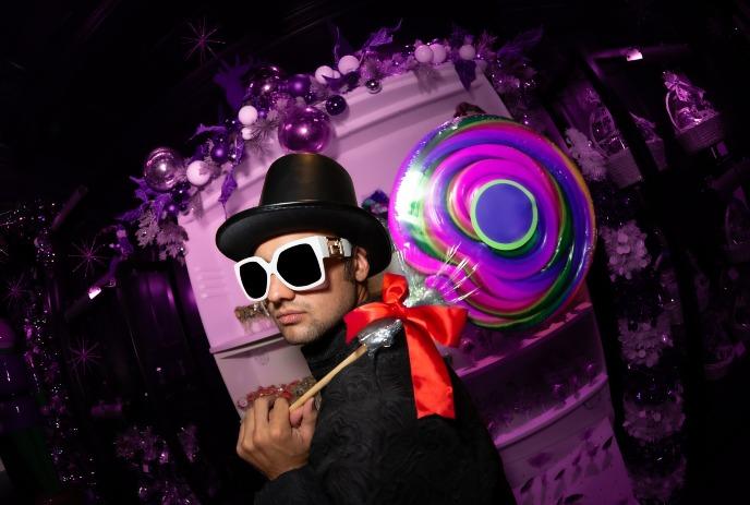 Wonky Willa in a black outfit and top hat, holding a colorful lollipop.