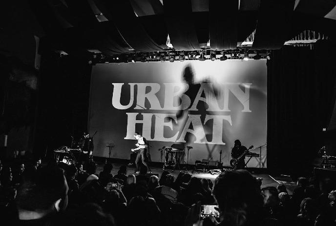A black and white photo of Urban Heat performing on stage in front of a crowd.
