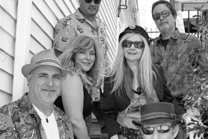 A black-and-white group photo featuring six people, some wearing hats and sunglasses, posing casually outdoors.