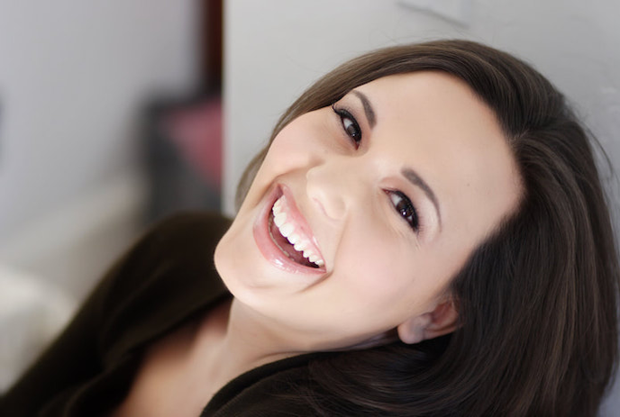 A woman with dark hair is smiling brightly, lying back with her head tilted slightly.