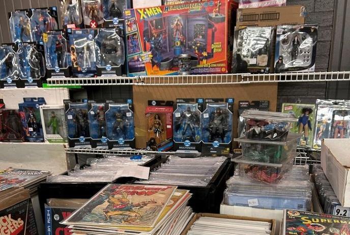 A display shelf filled with collectible action figures, comic books, and vintage superhero items. X-Men, DC, and Marvel.