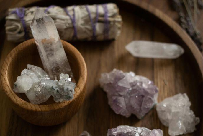 Various white and purple crystals and a smudge stick on a wooden surface.