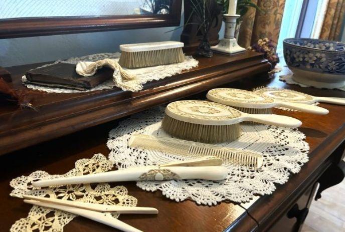 A vintage vanity set with intricately designed brushes, combs, and lace doilies displayed on a wooden dresser with a mirror.