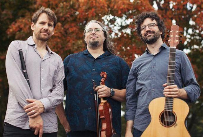 Three artists of the band standing and smiling for a picture while holding their instruments.