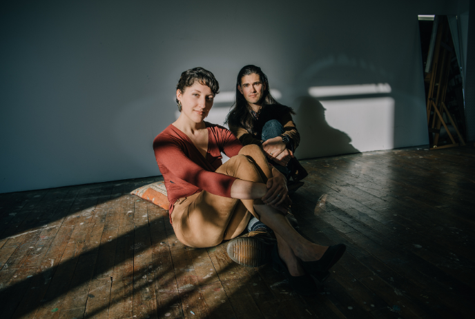 Two womans sitting on a wooden floor with sunlight streaming through a window, creating a warm and cozy atmosphere