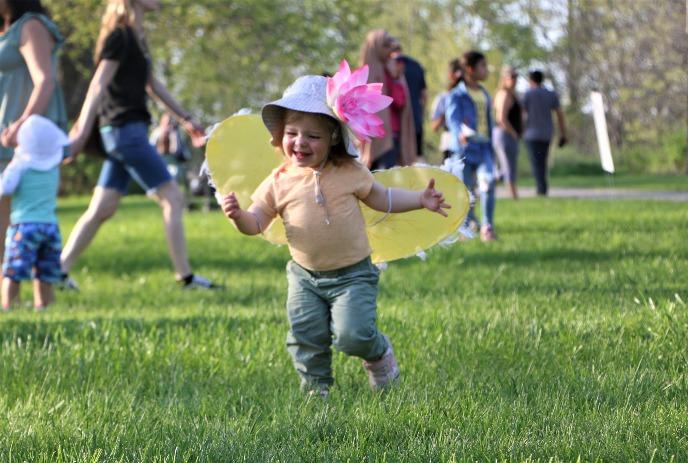 A young toddler playing in the grass with other toddlers and adults.