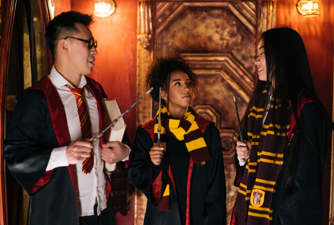 3 people wearing wizarding costumes and holding wands.