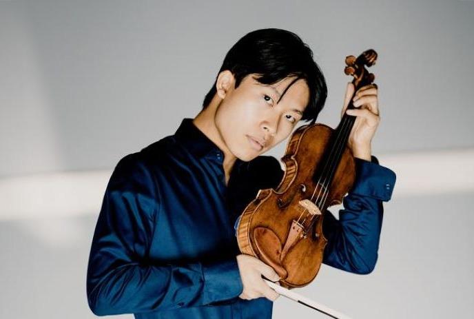 Kerson Leong wearing a dark blue shirt, holding his violin.