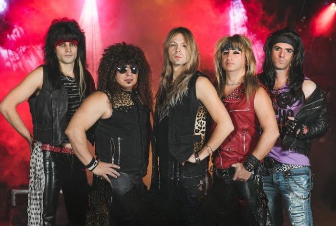 A group of 5 music artists with long hairs, wearing costumes under red smokey lights.