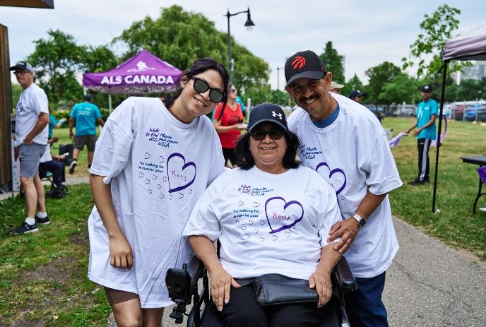 3 People wearing walk to end ALS shirts, two standing and the middle one in a wheelchair.