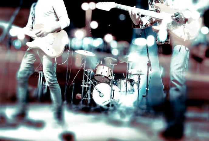 A red background with a white silhouette of a person playing an electric guitar the right side.