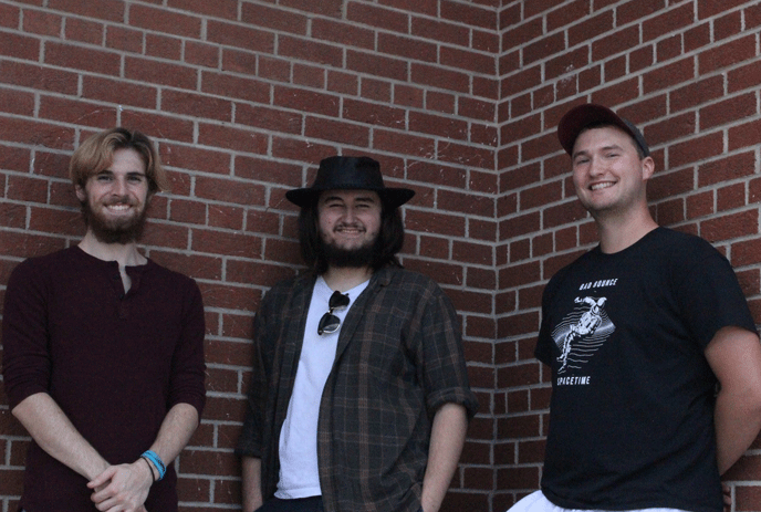 The 3 band members of Bad Bounce, posing against a brick wall, smiling.
