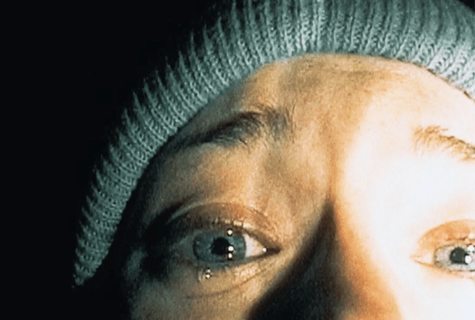 A close-up of a person’s eye, partially covered by a beanie, reflecting light. The image has a mysterious and intense feel.