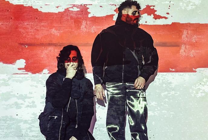 Artists posing in black outfits with red stripe under a white background.