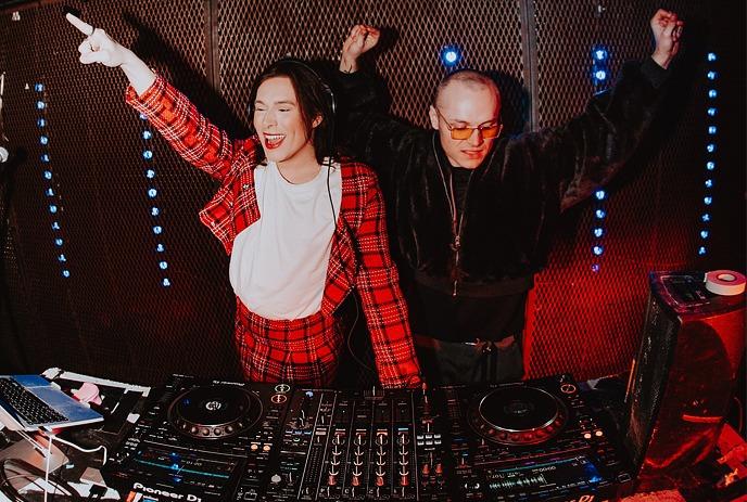 Two DJ's playing their music system while enjoying the atmosphere under a dark background and blue light stripes.