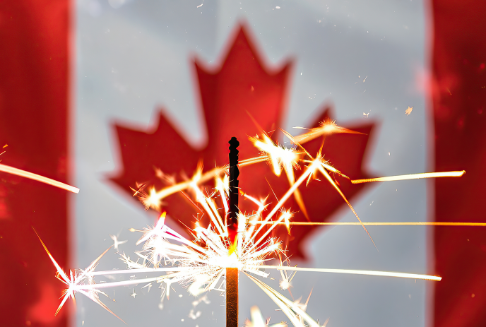 A sparkler lit in front of a blurred Canadian flag.