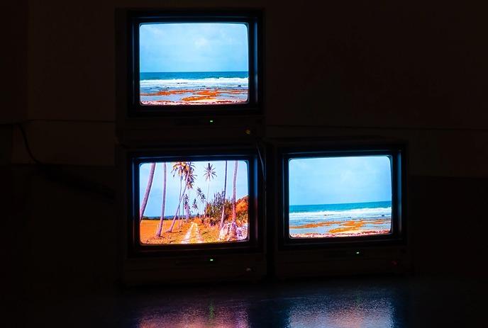 Three vintage CRT televisions stacked, each displaying a beach scene.