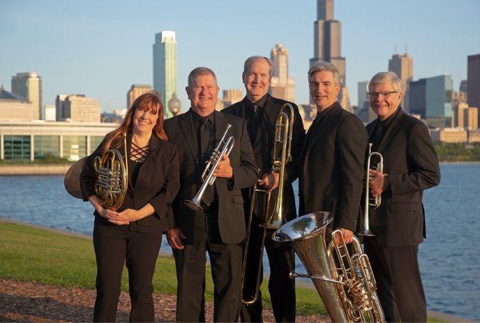 Brass quintet smiling for the picture with their instruments under a city skyline in the background