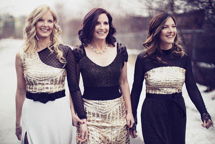 The three Ennis Sisters, dressed in black and gold, walking along a road together.