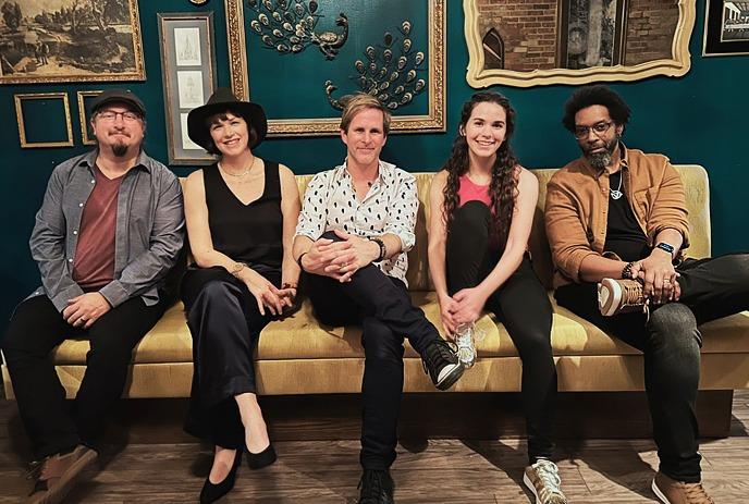 The 5 members of Classic Troubadours sitting together on a beige couch facing the camera, smiling.