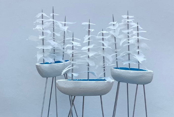 Three miniature sailboats with tiered white sails and blue interiors, displayed on black stands against a light background.