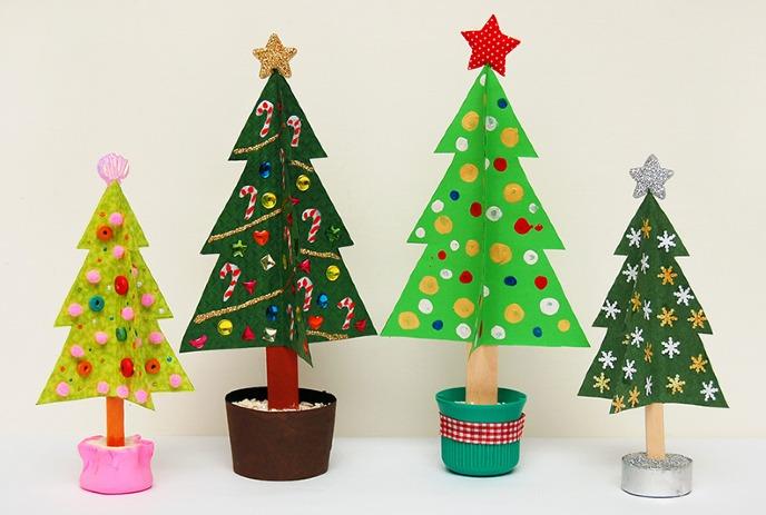 Four uniquely decorated handmade Christmas tree crafts, each with various ornaments and different bases, displayed in a row.