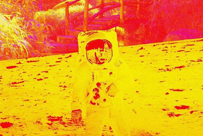 Heat map of an astronaut on a sandy terrain with a bridge behind; vivid red and yellow.