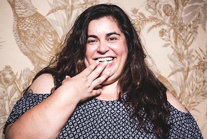 Debra DiGiovanni putting her hand over her face while laughing, in front of a floral pattern wall.