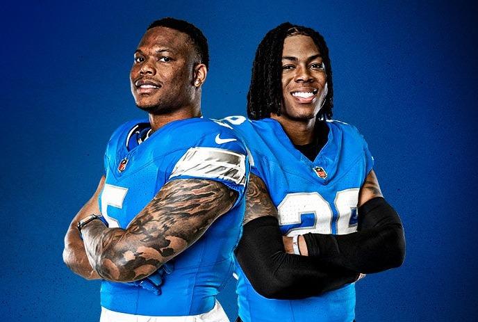 Two Detroit Lions players, standing side by side smiling, wearing their uniforms.