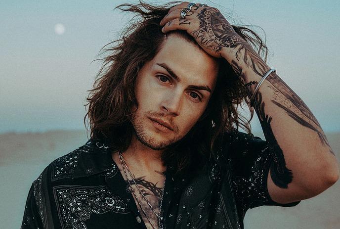 A headshot of Dillon James, in front of a sandy area at sunset.