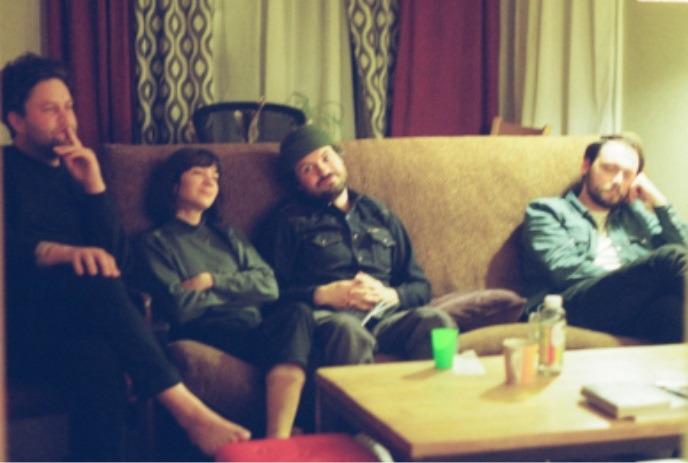 Four people sit on a couch with their faces obscured, creating a sense of anonymity and mystery in the scene.