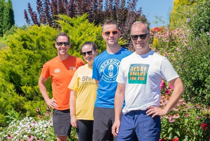 Four individuals standing in a garden with colorful flowers and greenery, wearing casual attire