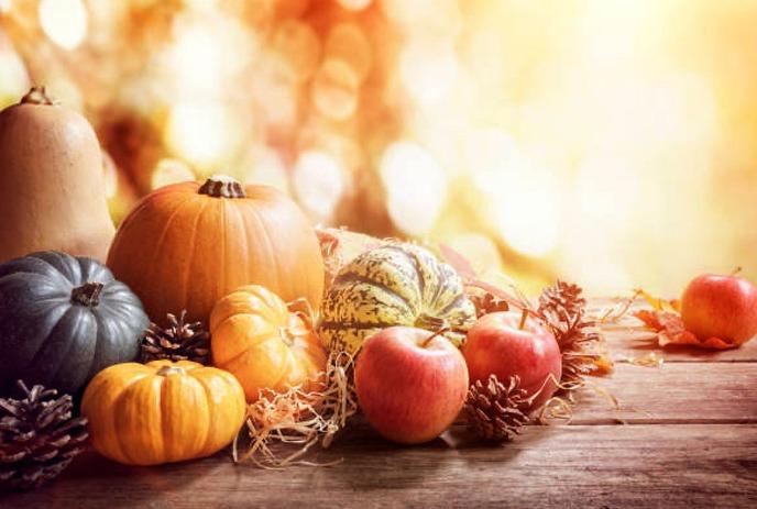 A cozy autumn scene with a pie, knitted sweater, canned preserves, and sunflowers in front of a scenic fall landscape.