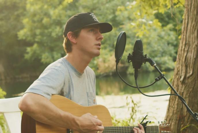 Dylan Gossett playing guitar outside in nature, singing into a microphone.