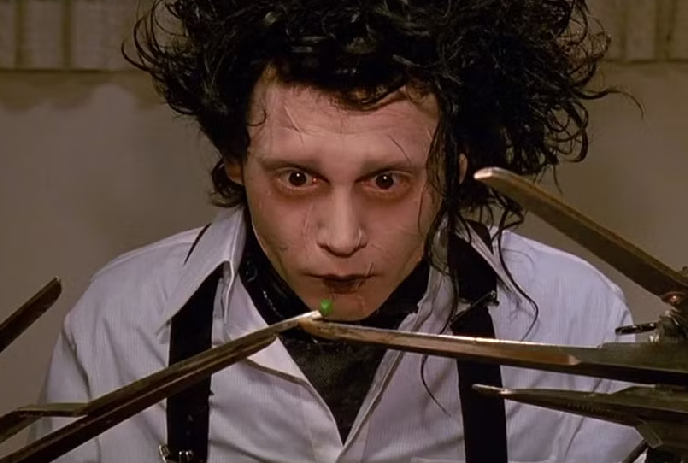 A person with curly hair wearing black suspenders and a white shirt with scissors for hands, evoking Edward Scissorhands.