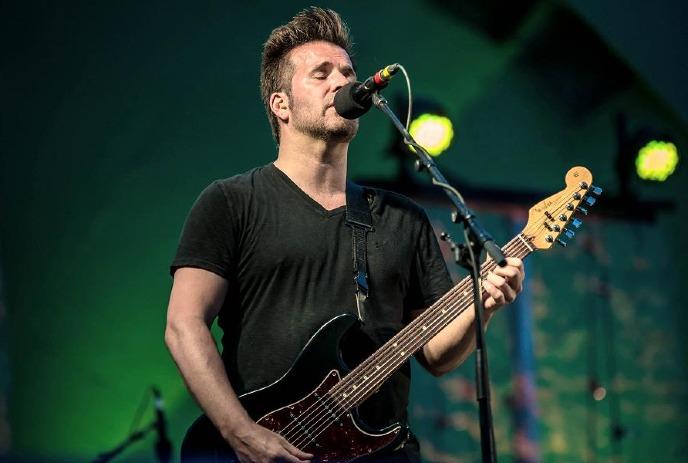 Edwin of I Mother Earth performs on stage, singing into a microphone while playing a black electric bass guitar.