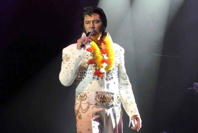 Tim 'E' Hendry singing with a microphone on stage, in costume as Elvis.