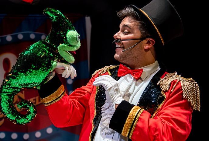 Person onstage holding a green puppet and talking to them.