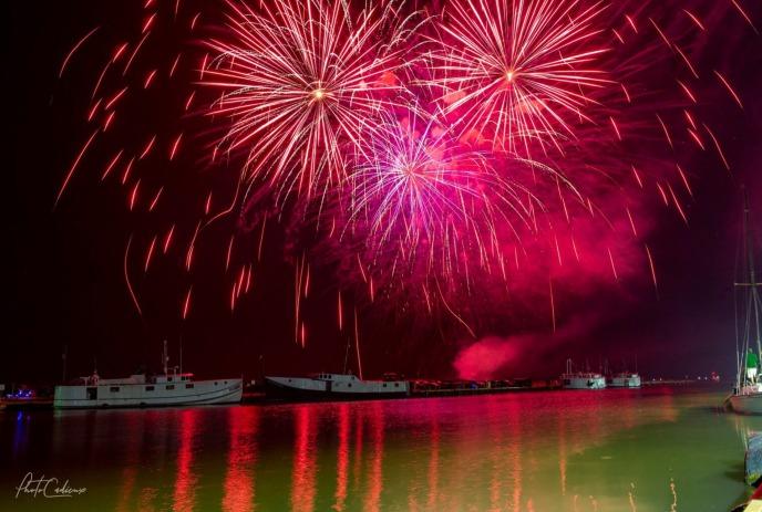 A vibrant display of red fireworks illuminates the night sky over a calm body of water, reflecting the bright colors.
