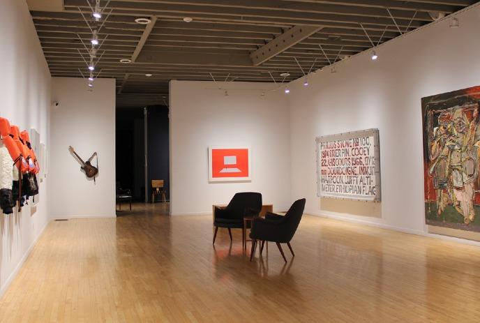 A modern art gallery with wooden floors, white walls, and spot lighting. Art pieces include wall-mounted life vests.