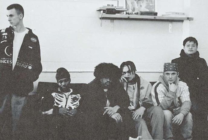 A black and white photo of 4 band members of Fresh Religion,  leaning on a car posing for the camera.