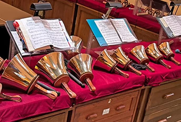 A lineup of various sizes of musical bells, with sheets of music on display