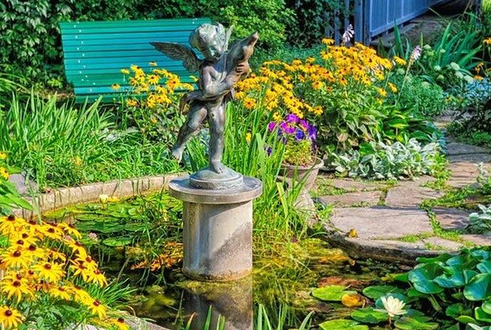 A vibrant garden scene with a statue of a cherub on a pedestal, surrounded by lush greenery and yellow flowers.