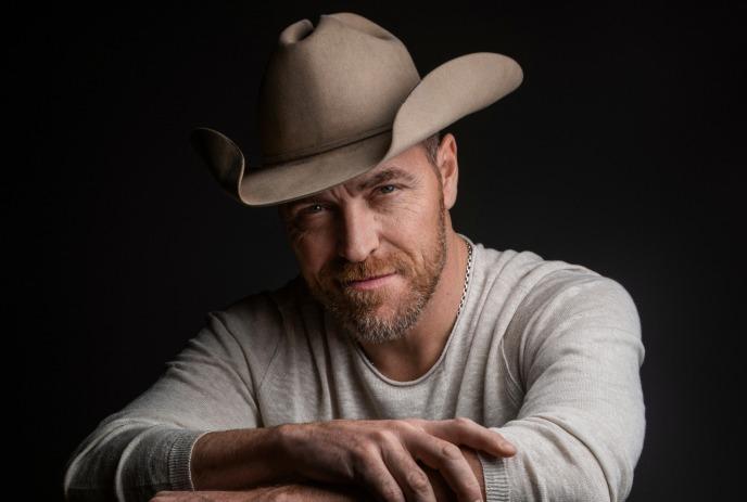 George Canyon wearing a cowboy hat, looking at the camera with his arms crossed.